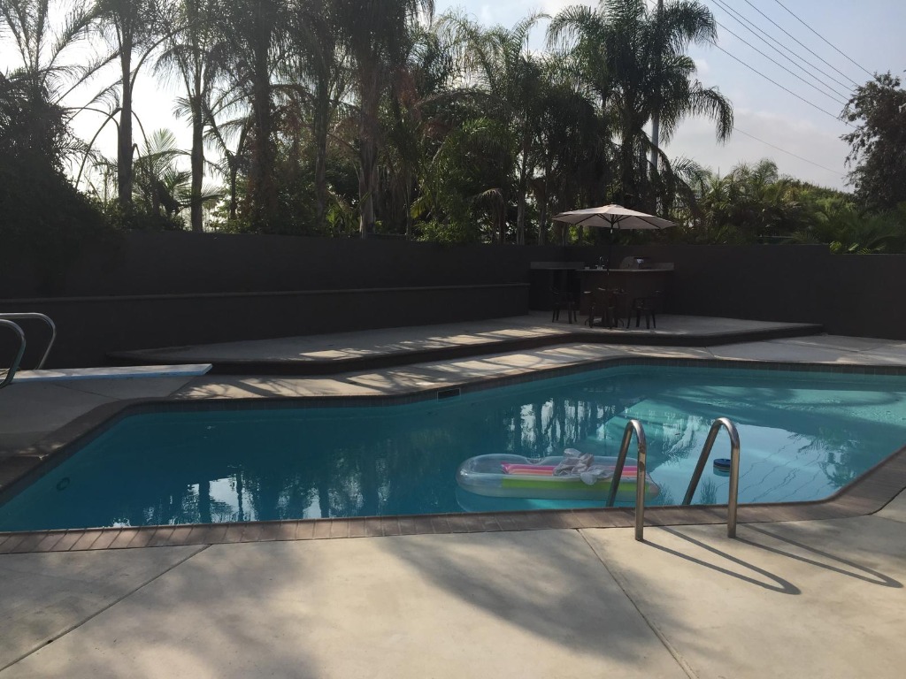 Sparkling swimming pool view with clean blue water, new coping, pool ladder, and poolside patio furniture