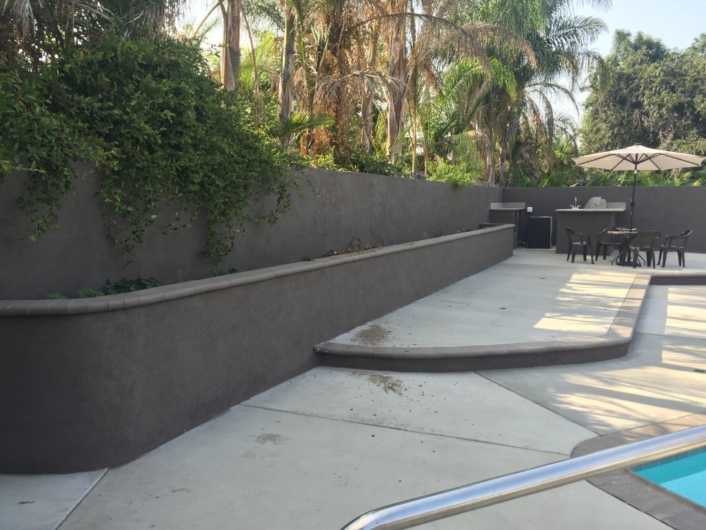 Custom curved stucco retaining wall with bullnose coping, concrete patio, and outdoor kitchen bar station